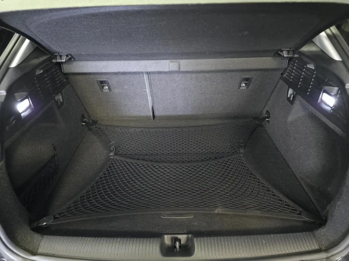 Coffre ouvert d'un Audi Q2 noir, montrant un filet de rangement et un intérieur entièrement noir avec éclairage latéral.