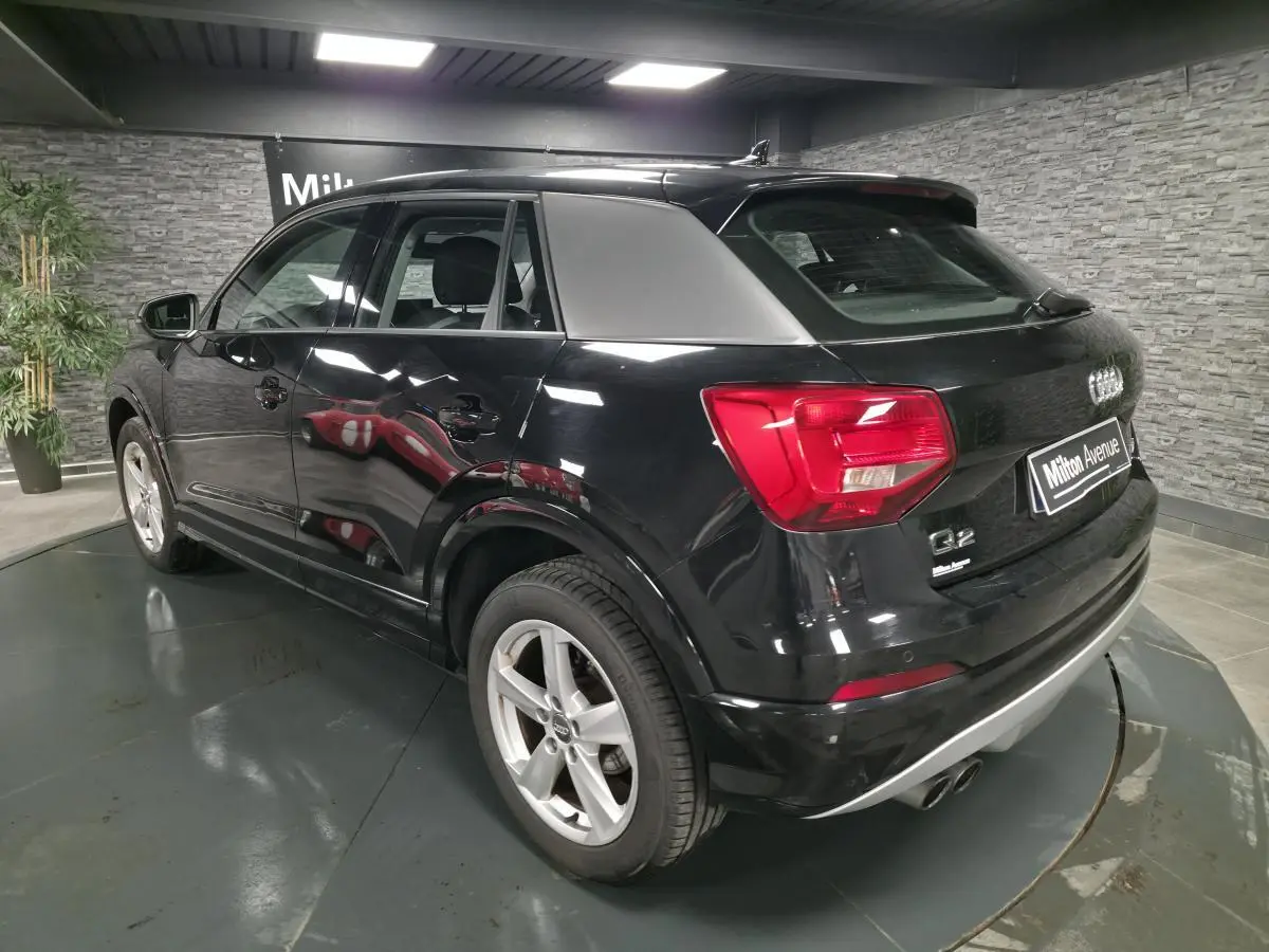 Audi Q2 noir en 3/4 arrière droit, avec jantes 5 branches et feux arrière rouges dans un showroom.