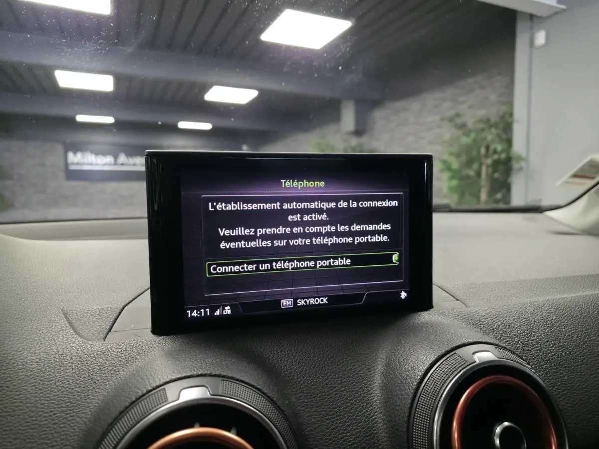 Écran MMI central affichant la connexion téléphone dans l'Audi Q2 1.4 TFSI noir, intérieur avec aérateurs cerclés rouges.