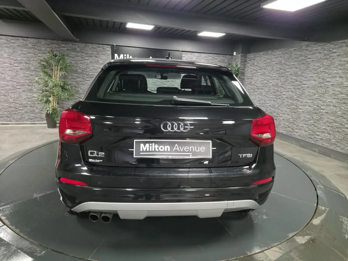 Vue arrière d'un Audi Q2 noir avec double sortie d'échappement à gauche et logo TFSI sur un plateau tournant intérieur.