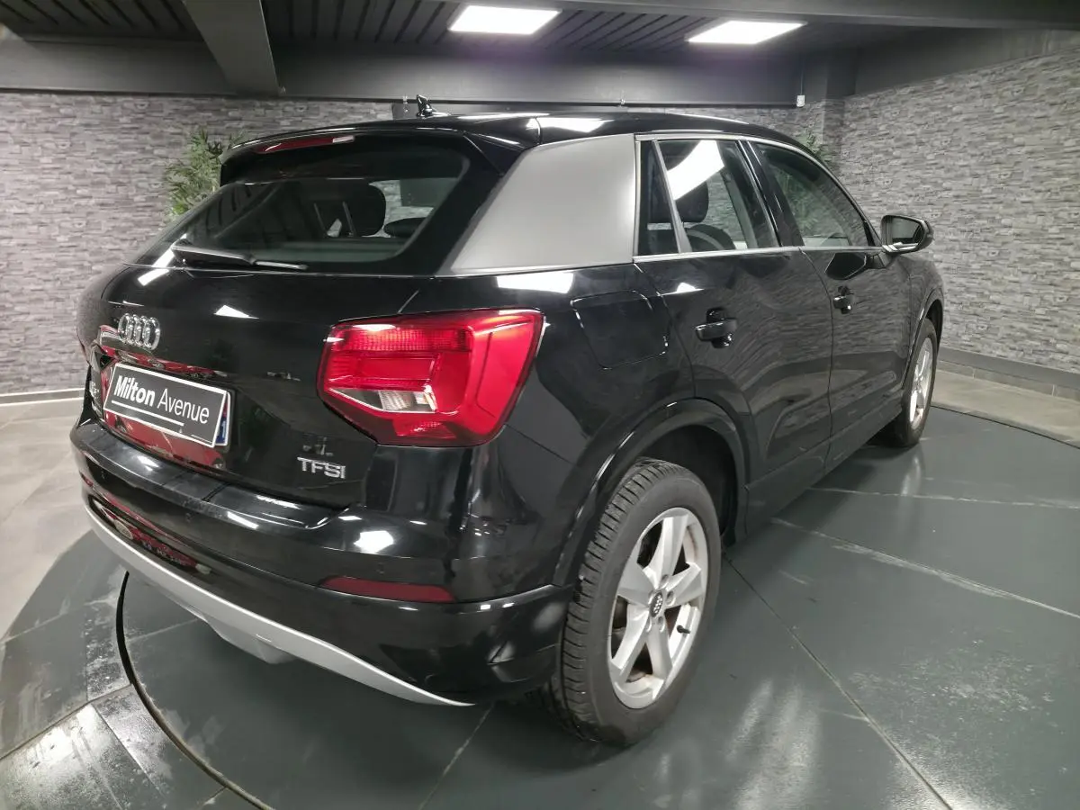 Audi Q2 noir vue 3/4 arrière droit avec toit argenté et feux arrière rouges en intérieur showroom.