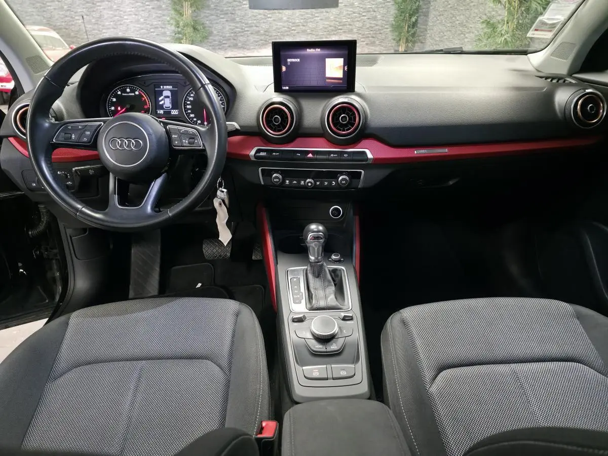 Intérieur Audi Q2 2017 noir, vue avant centrée sur tableau de bord avec applications rouges et console centrale automatique.
