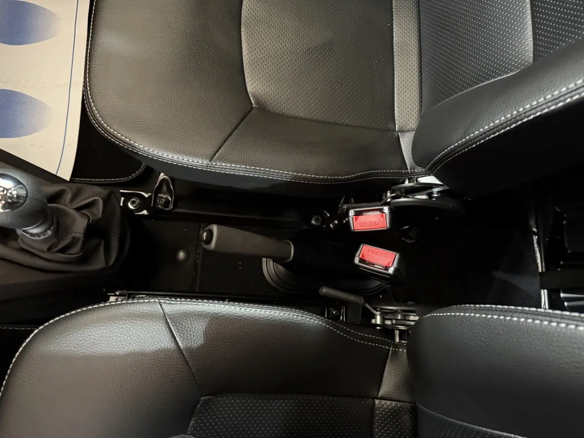 Vue plongeante sur les sièges noirs et la console centrale avec frein à main et ceintures rouges d'une Aixam Ambition 0.5 Crossover Premium.