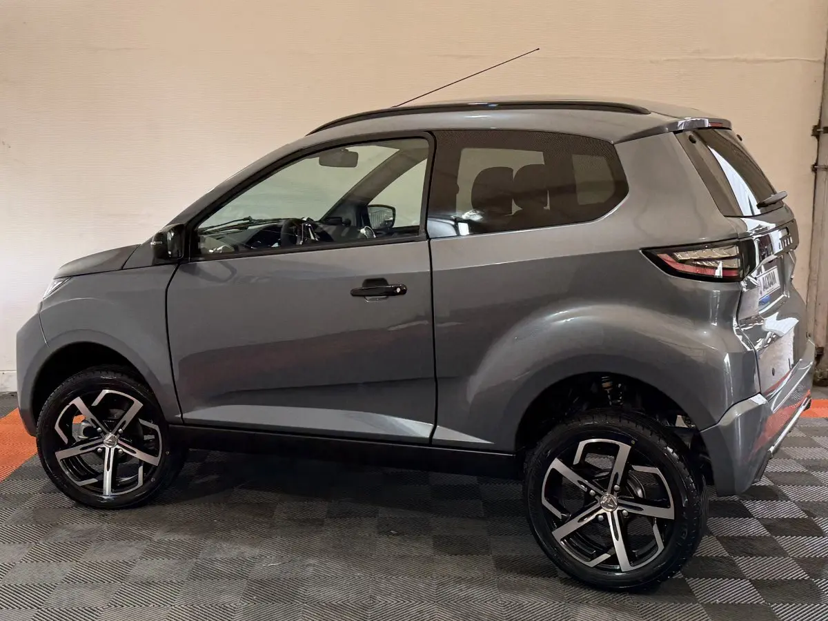 Vue de profil côté gauche d'une Aixam Ambition 0.5 Crossover Premium gris foncé avec jantes alliage et rétroviseur caméra.