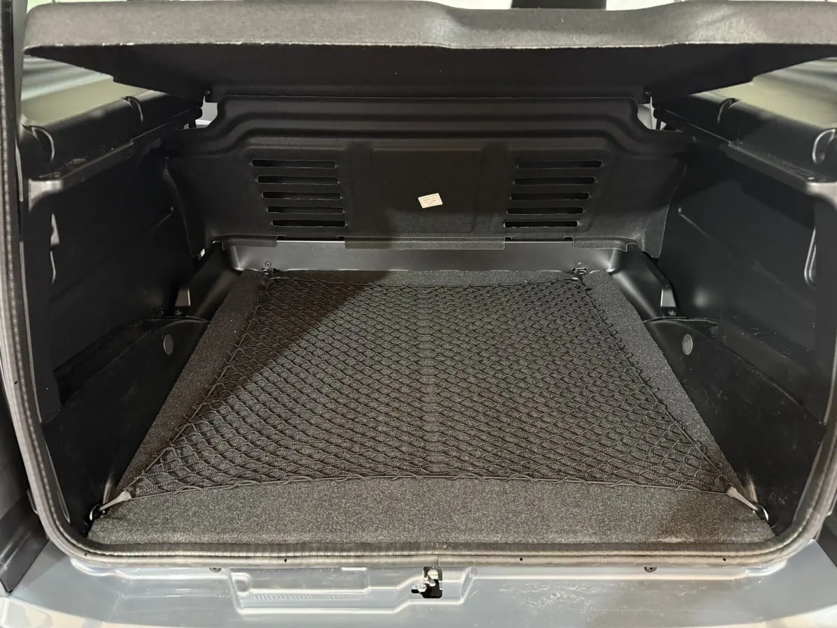 Coffre ouvert vu de l'arrière d'une Aixam Ambition 0.5 Crossover Premium gris foncé, avec filet de rangement au sol.