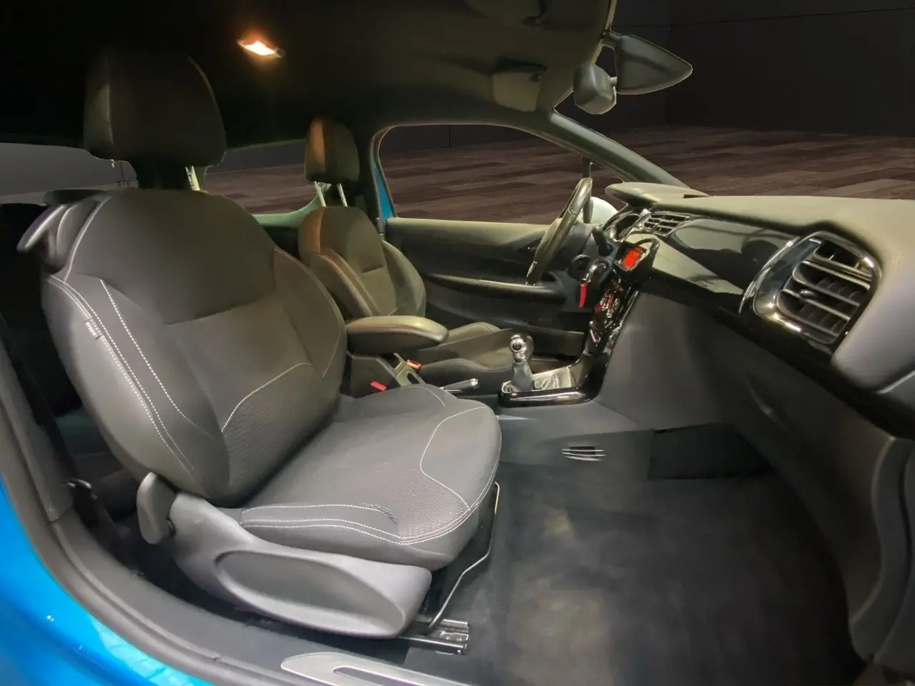 Vue intérieure côté conducteur de la Citroën DS3 bleu avec sièges tissu noir et tableau de bord moderne.
