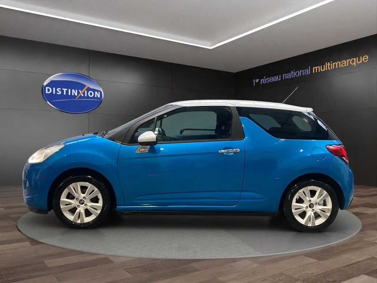 Profil droit d'une Citroën DS3 bleu avec toit blanc, en intérieur sur un plateau rotatif, mettant en valeur ses jantes blanches.