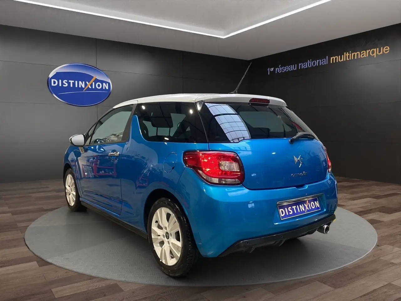 Citroën DS3 bleu avec toit blanc, vue 3/4 arrière droit, jantes blanches et feux arrière rouges visibles.