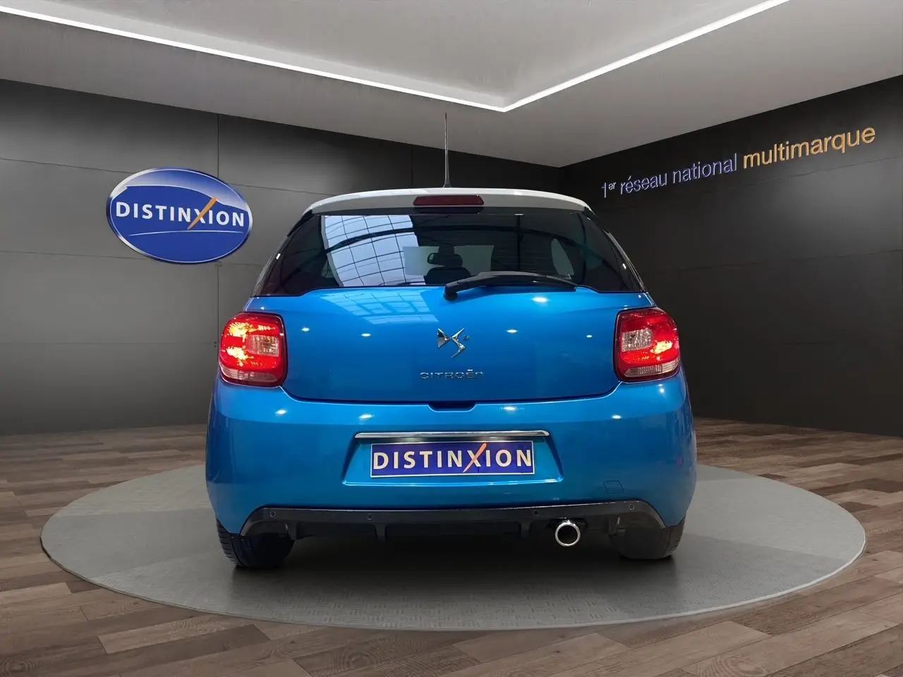 Vue arrière d'une Citroën DS3 bleu avec toit blanc, feux allumés et sortie d'échappement chromée visible.