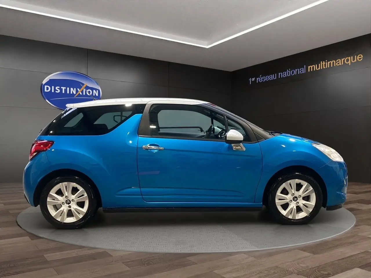 Profil droit d'une Citroën DS3 bleu avec toit blanc, jantes alliage et rétroviseurs blancs, en présentation showroom.