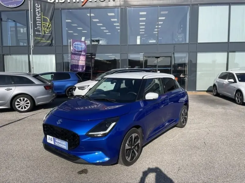 Suzuki Swift 1.2 Dualjet Hybrid bleu métal vue 3/4 avant droit avec toit et rétroviseurs blancs, en extérieur devant un showroom.