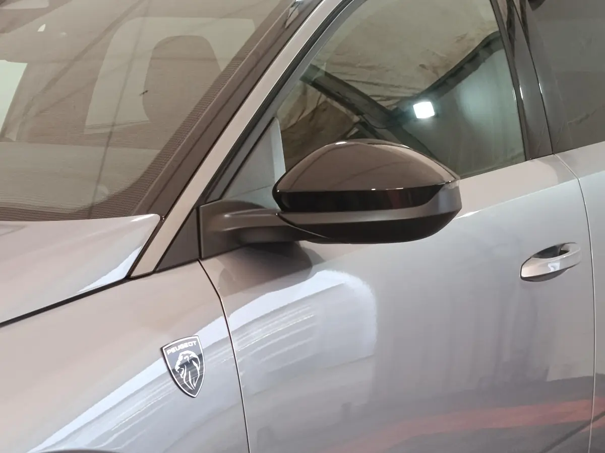 Gros plan sur le côté gauche gris clair du Peugeot 5008 2026, avec rétroviseur noir et logo Peugeot visible.