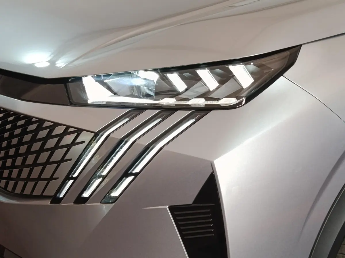 Gros plan sur le phare avant droit et la calandre en losange du Peugeot 5008 gris clair, version 2026.