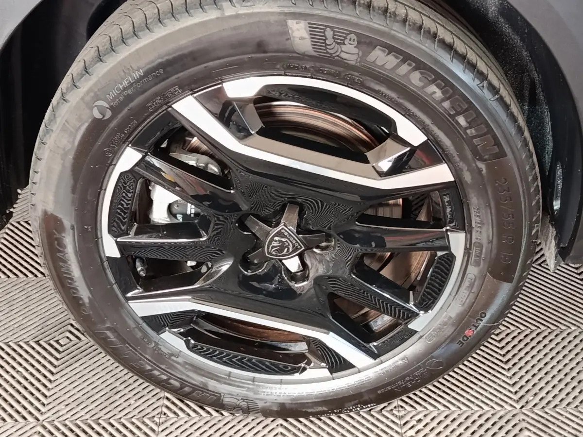 Gros plan sur la roue avant droite d’un Peugeot 5008 gris clair, jante alliage noire et argent avec logo lion central.