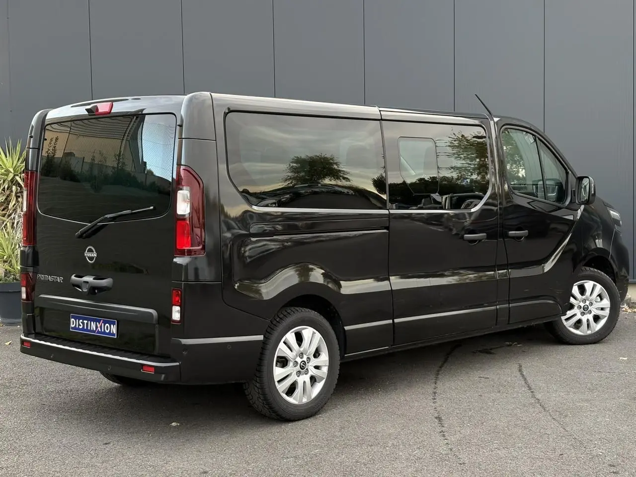 Nissan Primastar Combi noir métal vu en 3/4 arrière droit, hayon vitré et vitres latérales teintées.
