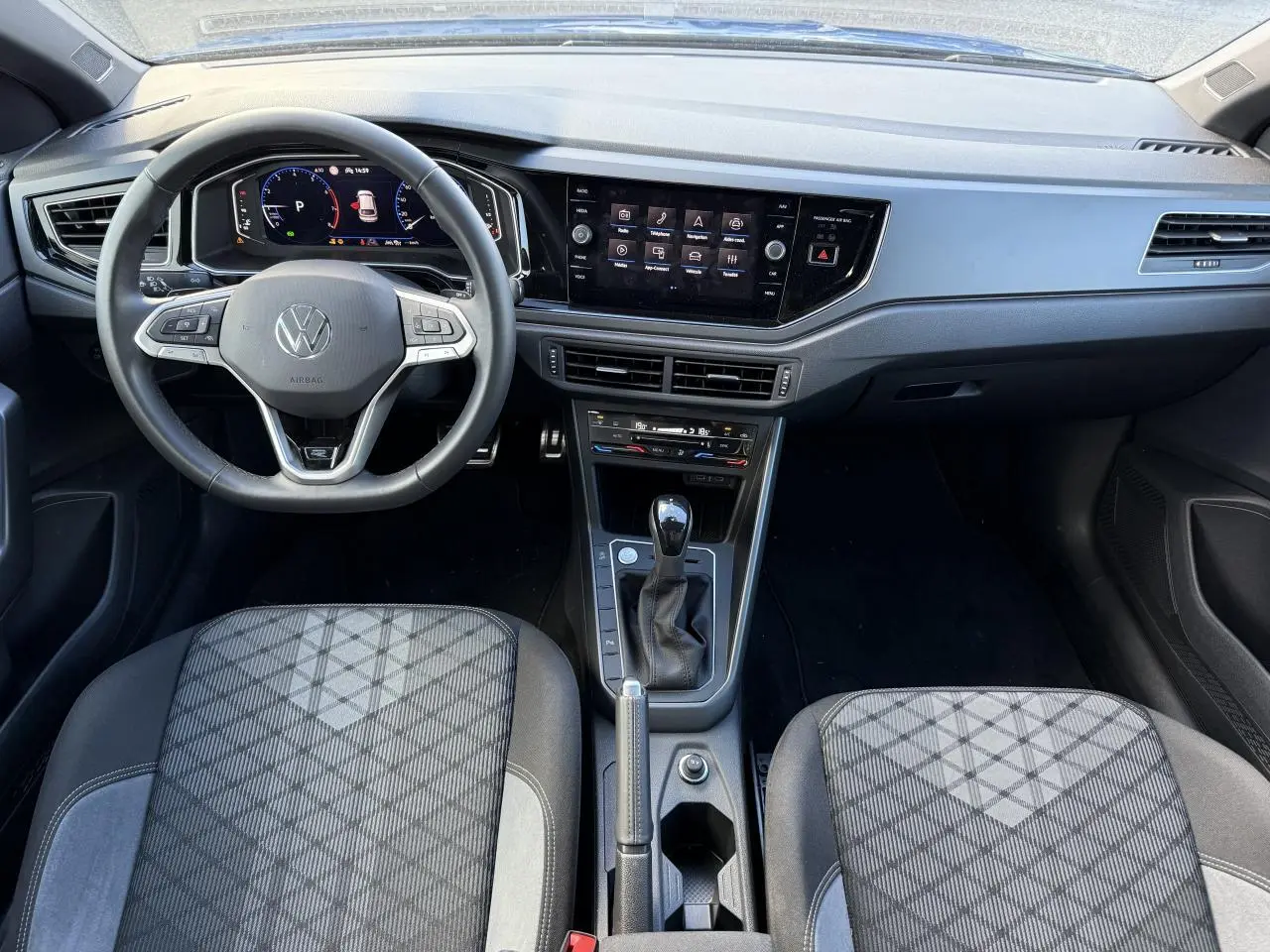 Vue intérieure frontale du tableau de bord et volant cuir multifonctions du Volkswagen Taigo 2025 avec console centrale et sièges tissu noir à motifs.