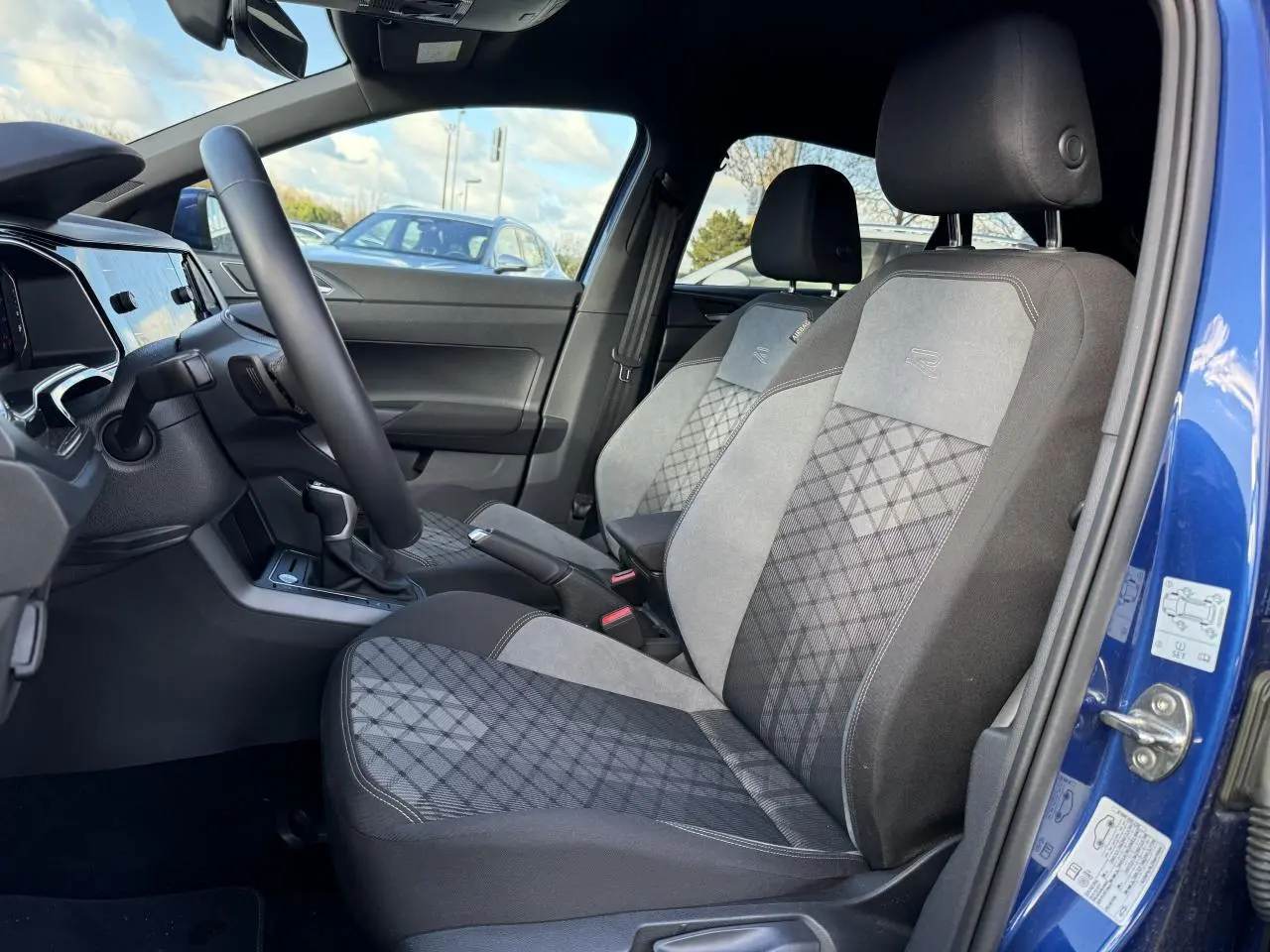 Vue intérieure côté conducteur du Volkswagen Taigo bleu récif, sièges Sport-Confort avec logo R et tissu à motif géométrique.