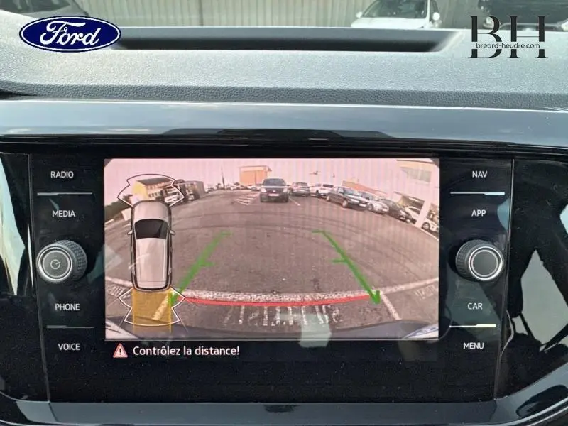 Écran de caméra de recul montrant une vue arrière avec lignes de guidage vertes et rouge sur un Volkswagen T-Cross noir nacré.