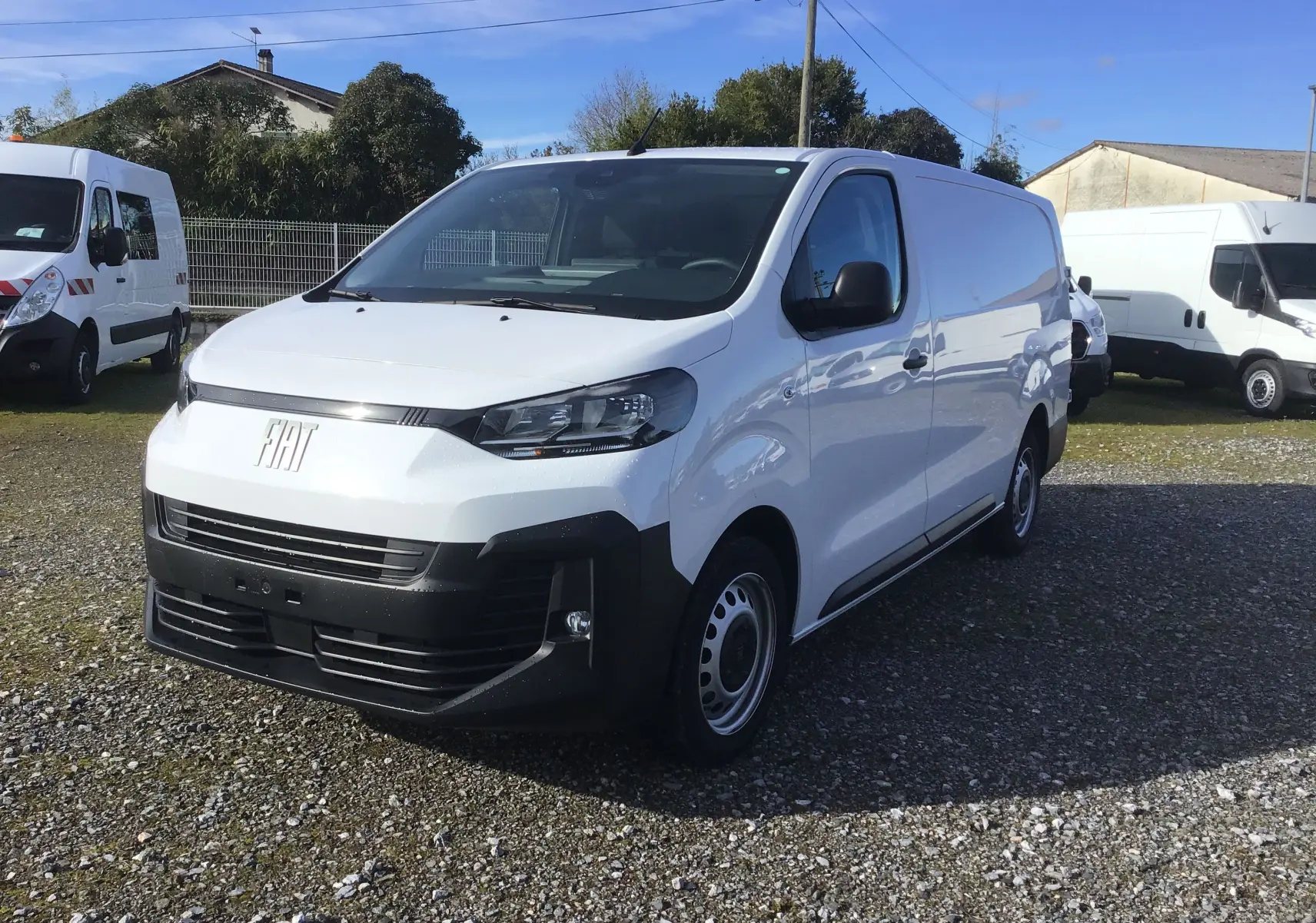 Vue 3/4 avant droite d’un FIAT Scudo Fourgon blanc 2024 avec pare-chocs noir et jantes acier, stationné sur gravier.