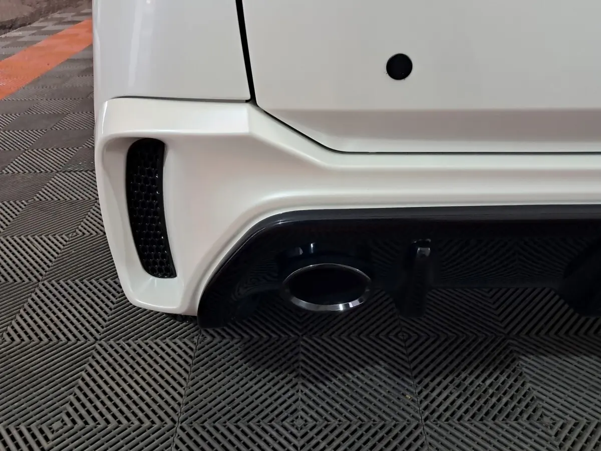 Gros plan sur le bas arrière droit blanc de l'AIXAM AMBITION 0.5 CITY COUPE GTI avec sortie d'échappement et diffuseur noir.