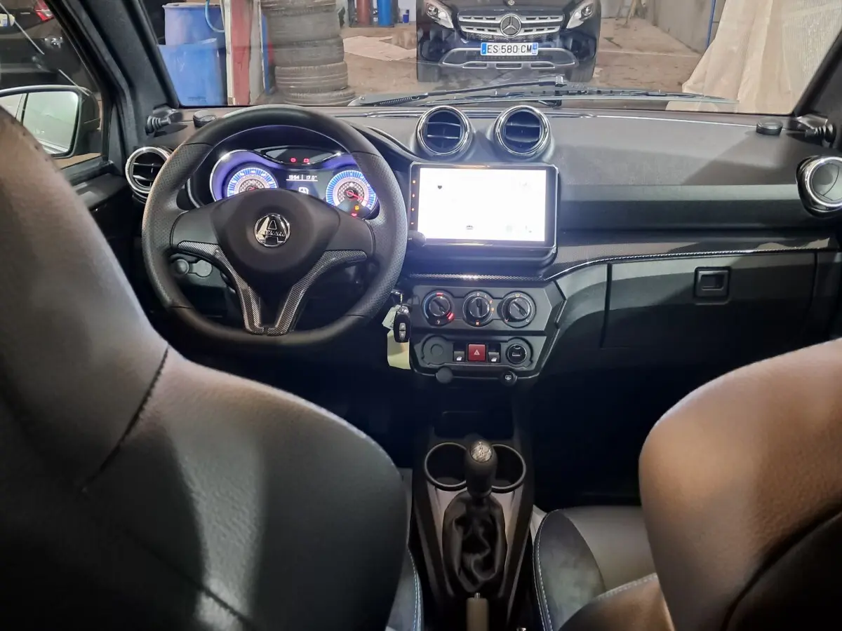 Vue intérieure avant de l'AIXAM Ambition 0.5 City Coupe GTI 2026, tableau de bord noir avec écran tactile central lumineux.