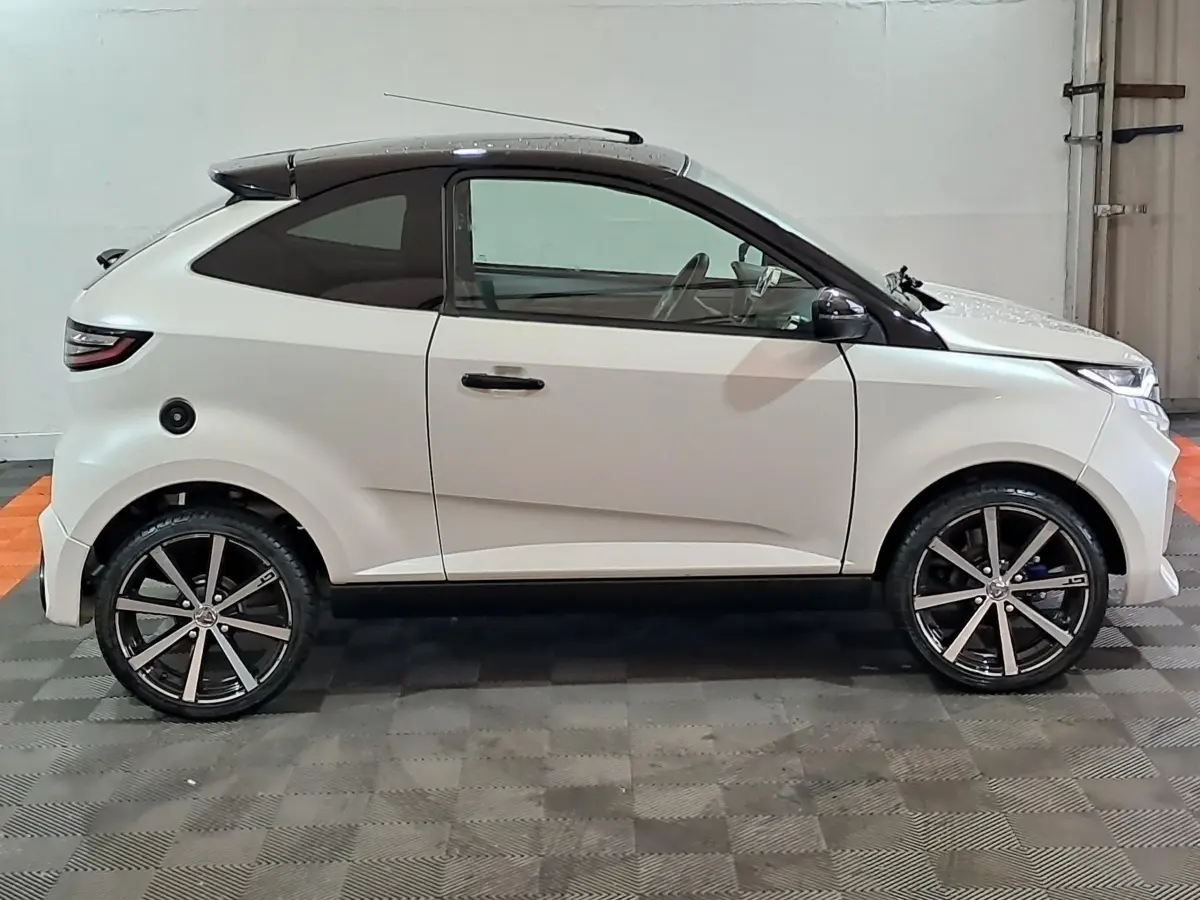 Vue de profil côté gauche d'une AIXAM AMBITION 0.5 CITY COUPE GTI blanche avec rétroviseur caméra côté conducteur.