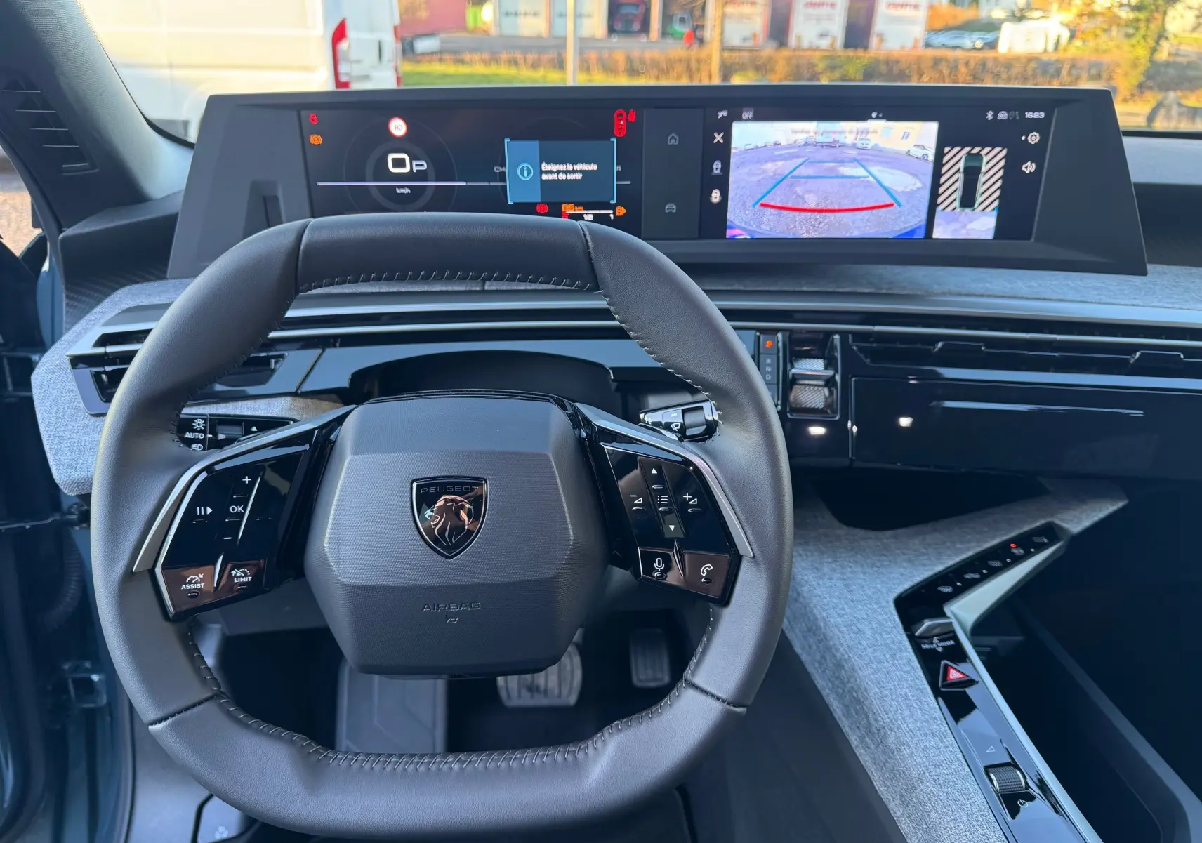 Vue intérieure centrée sur le volant cuir du Peugeot 3008 Hybrid 2025 avec tableau de bord numérique et caméra de recul affichée.