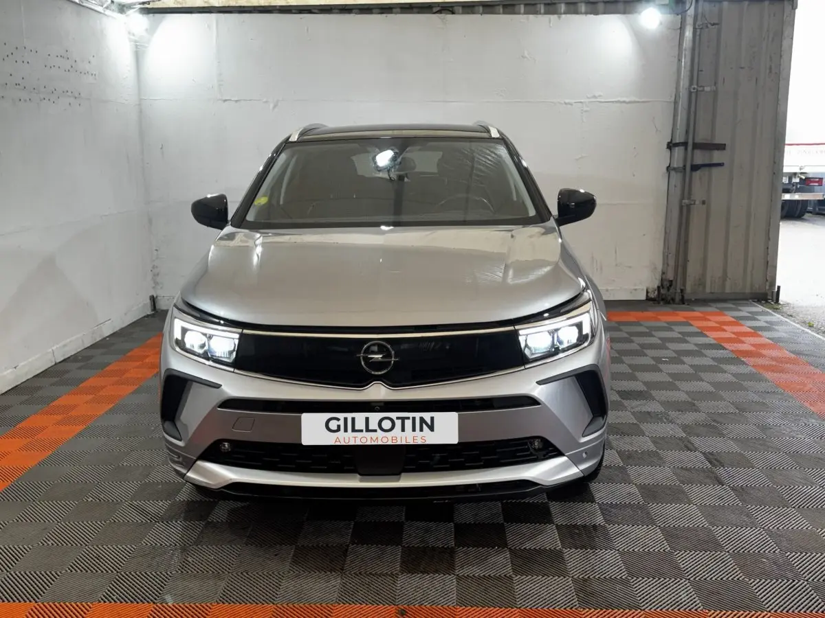 Vue frontale d'un Opel Grandland gris clair avec phares LED allumés dans un garage.
