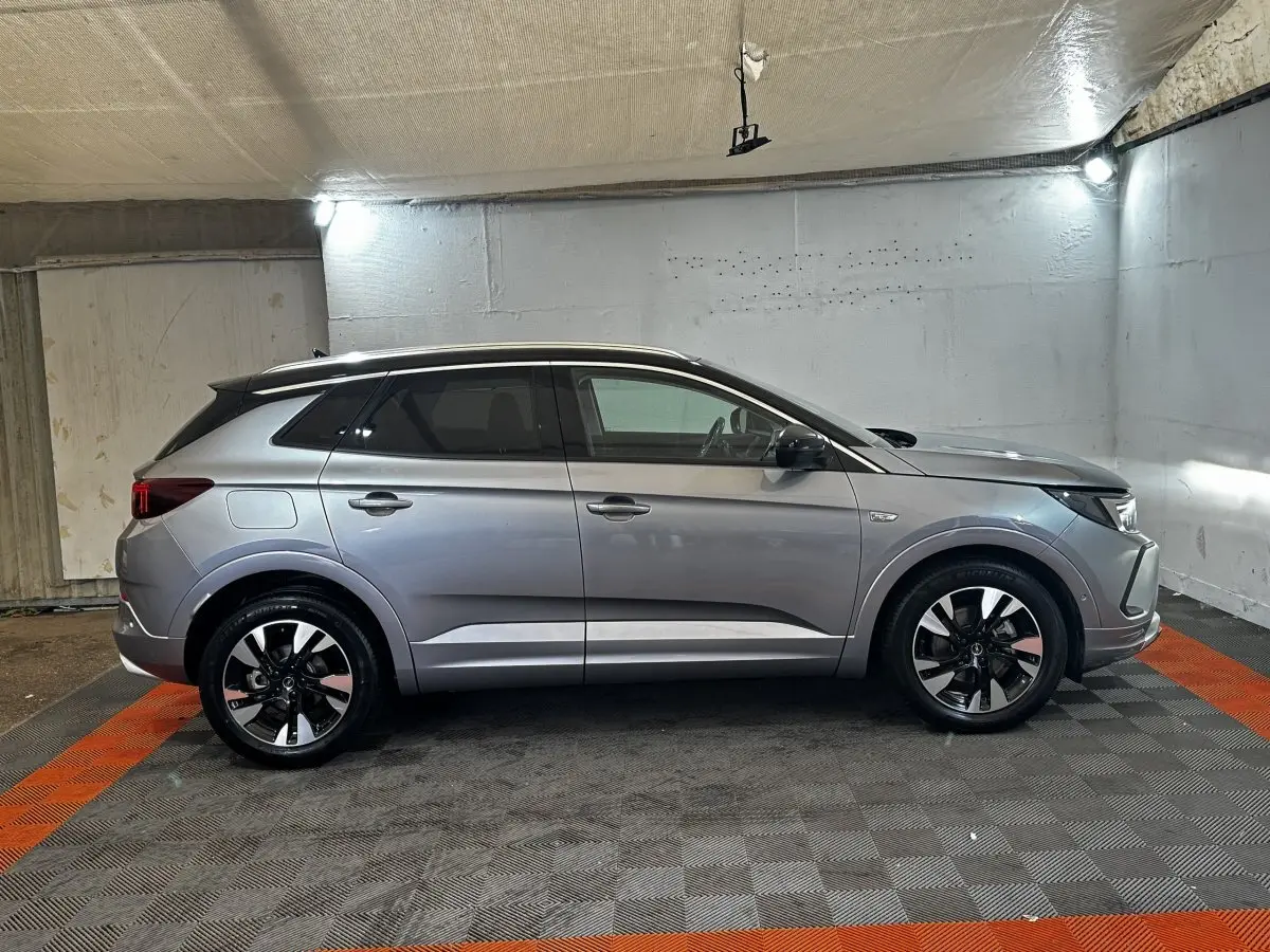 Vue de profil côté gauche d'un Opel Grandland gris clair 2022 avec jantes bicolores et toit noir dans un garage.