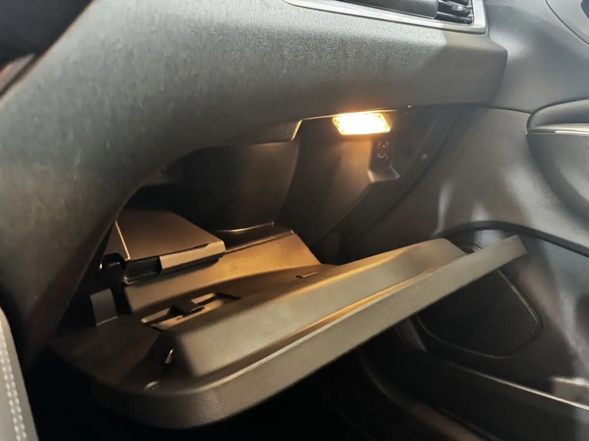 Gros plan sur la boîte à gants ouverte avec éclairage intérieur dans l’habitacle sombre d’un Opel Grandland 2022.
