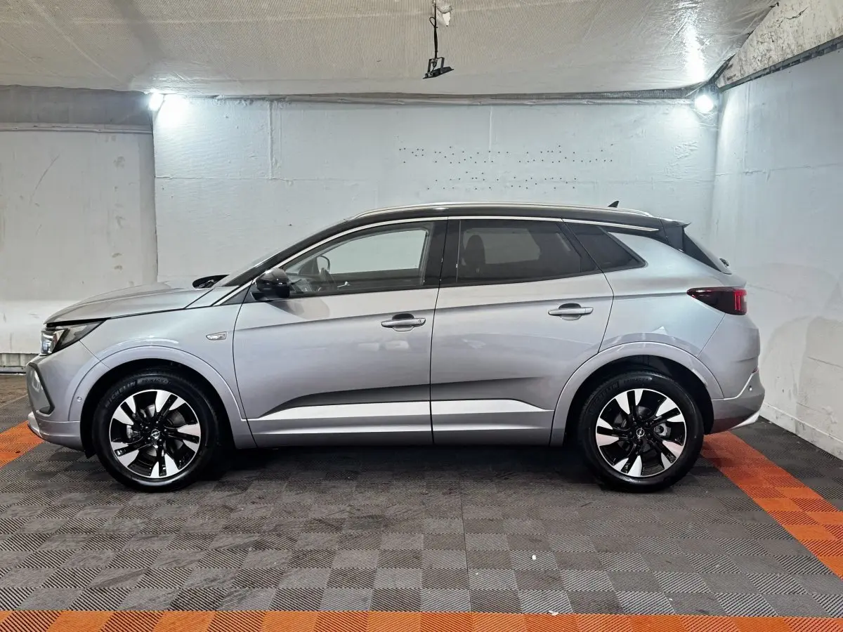 Opel Grandland gris clair vu de profil côté gauche, avec jantes bicolores et toit noir contrastant.