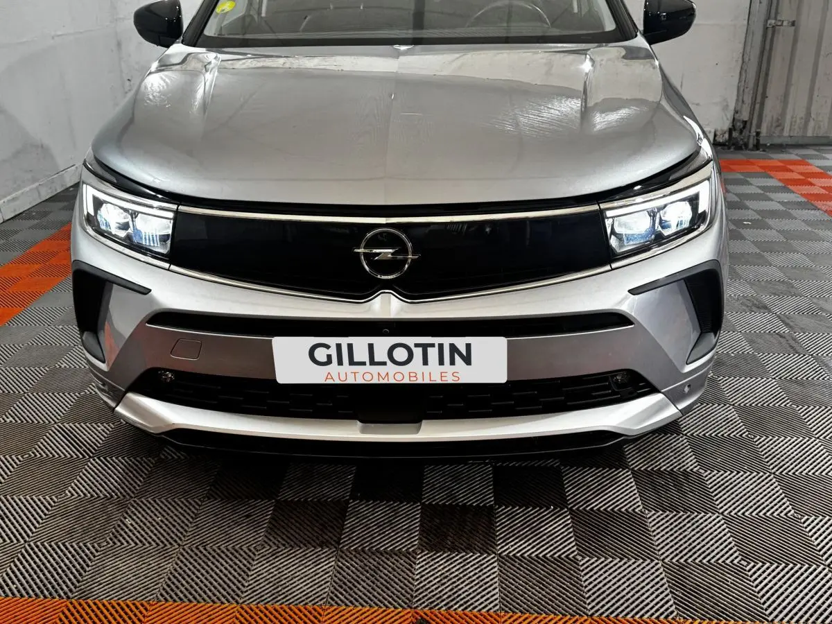Vue frontale d'un Opel Grandland gris clair avec phares LED allumés et calandre noire brillante.
