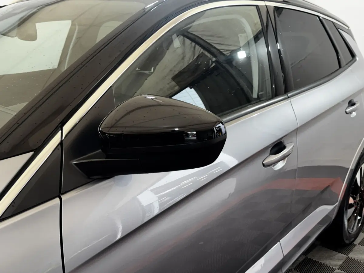 Vue côté gauche rapprochée d’un Opel Grandland gris clair avec rétroviseur noir brillant et poignées de porte assorties.