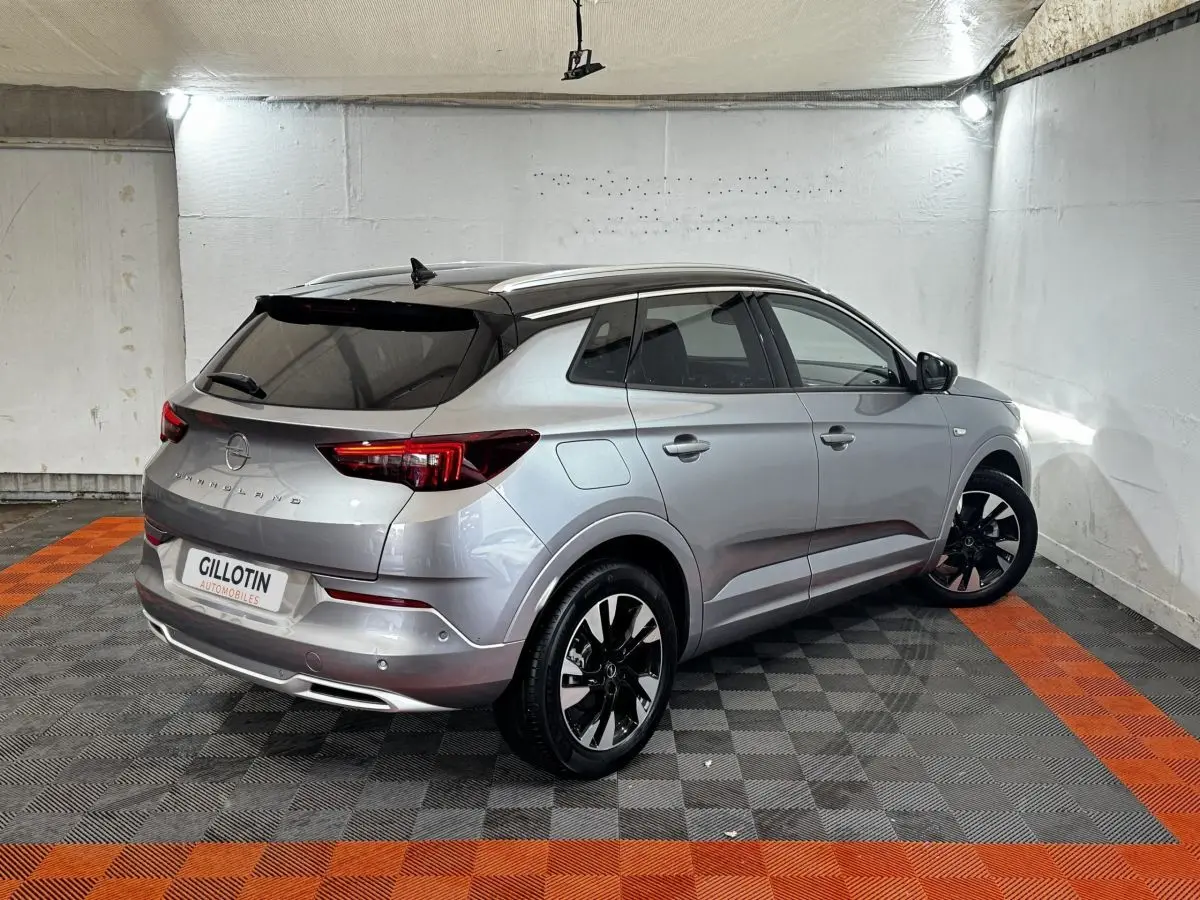 Opel Grandland gris clair, vue 3/4 arrière droit, jantes noires et toit noir contrasté en intérieur.