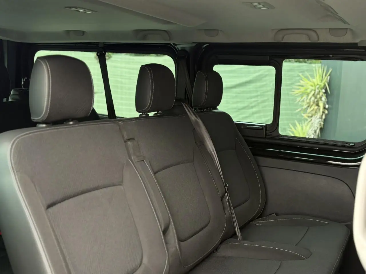 Vue intérieure côté droit sur la deuxième rangée de sièges noirs du Nissan Primastar Combi 2025 avec vitres coulissantes ouvertes.