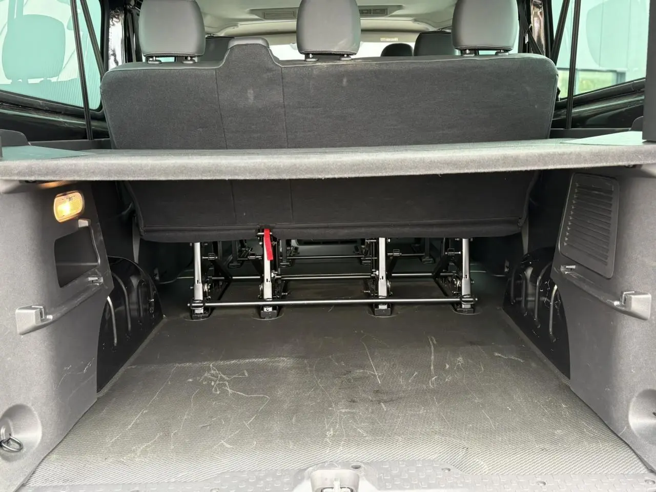 Coffre ouvert du Nissan Primastar Combi noir métal, vue arrière montrant la troisième rangée de sièges et le plancher de chargement.