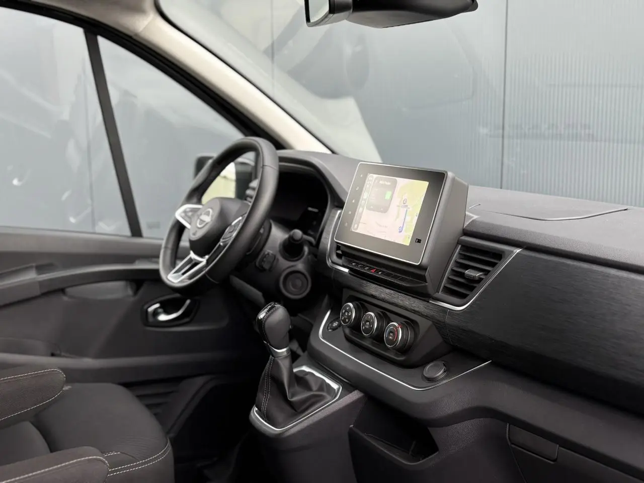 Intérieur du Nissan Primastar Combi 2025 vu côté conducteur, avec tableau de bord noir et écran tactile central.