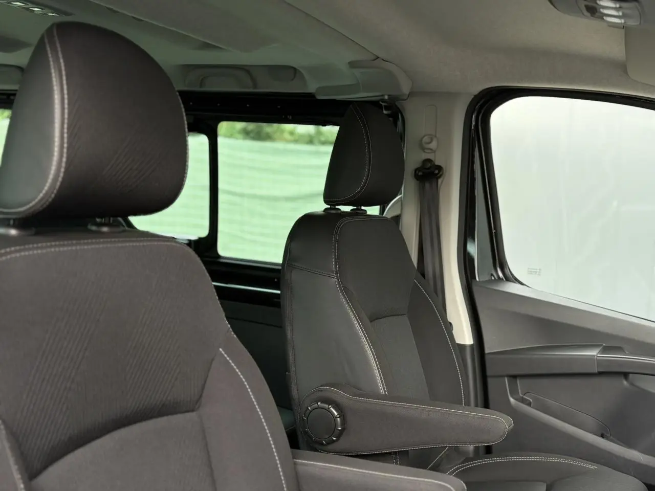 Intérieur du Nissan Primastar Combi 2025, vue côté droit sur sièges noirs avec accoudoirs et vitres latérales.