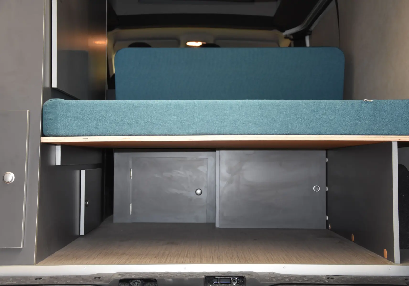 Vue intérieure arrière du Renault Trafic Combi blanc 2021, montrant un espace de rangement sous un siège bleu.