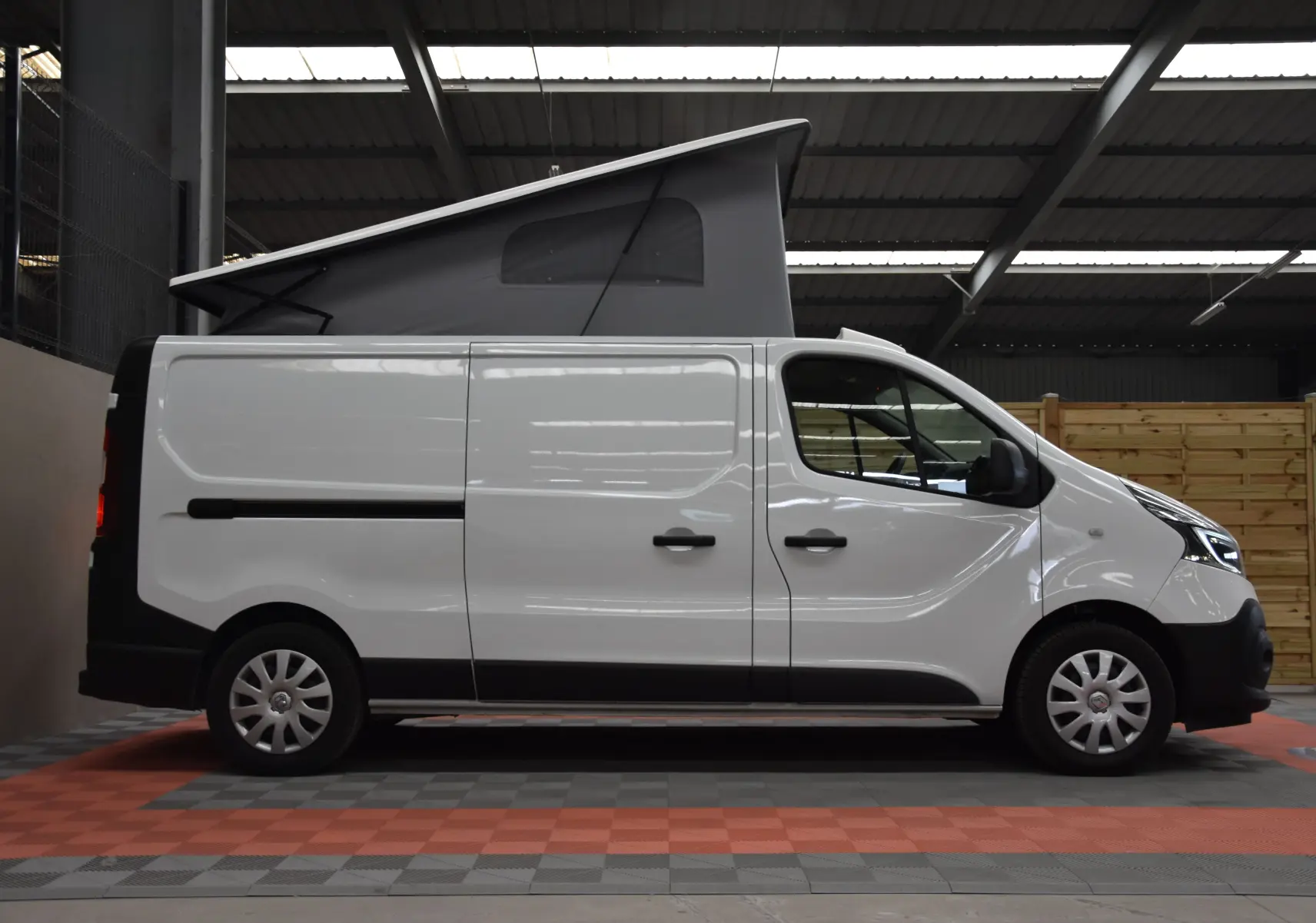 Profil droit d’un Renault Trafic Combi blanc 2021 avec toit relevé en tente grise, stationné en intérieur.