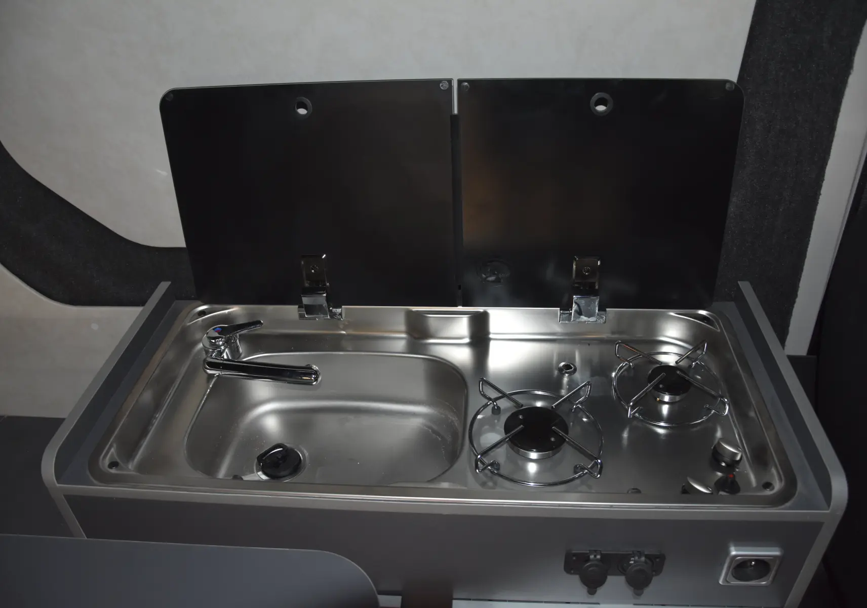 Plan rapproché sur l'évier et le réchaud inox intégrés dans l'aménagement intérieur du Renault Trafic Combi blanc.