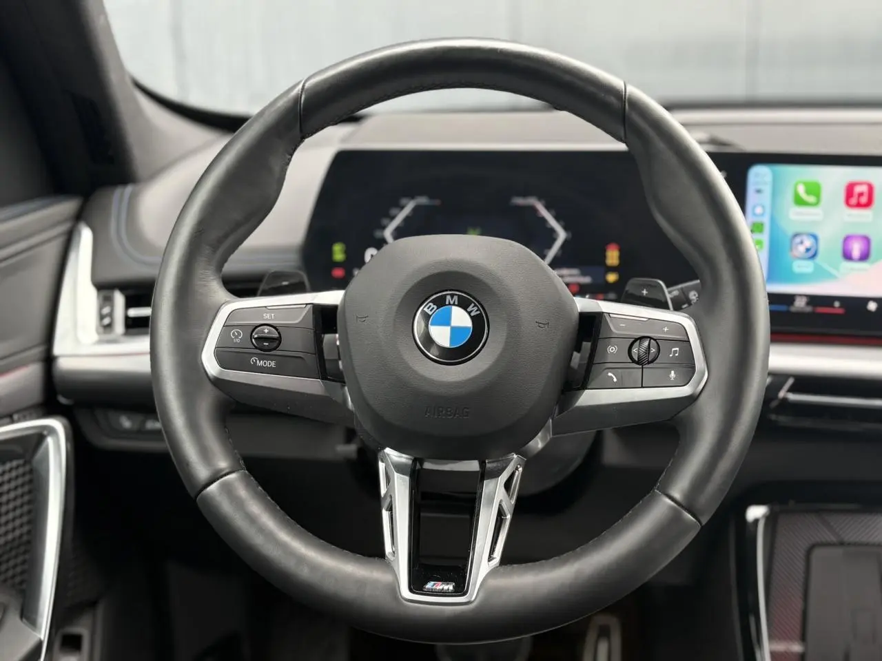 Volant M cuir noir de BMW X1 2025, vue frontale centrée sur les commandes multifonctions et tableau de bord numérique.