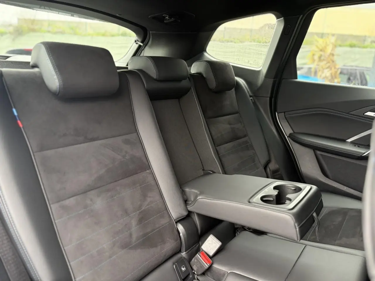 Vue intérieure arrière côté droit montrant les sièges Alcantara noirs avec accoudoir central et porte-gobelets du BMW X1 2025.