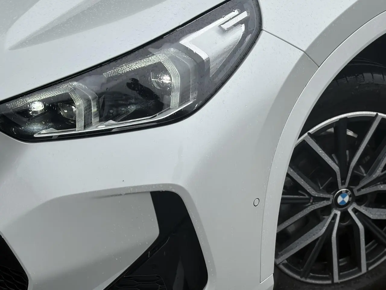 Gros plan sur l'avant droit blanc Mineral du BMW X1 2025 avec projecteur LED et jante alliage 18 pouces style M.