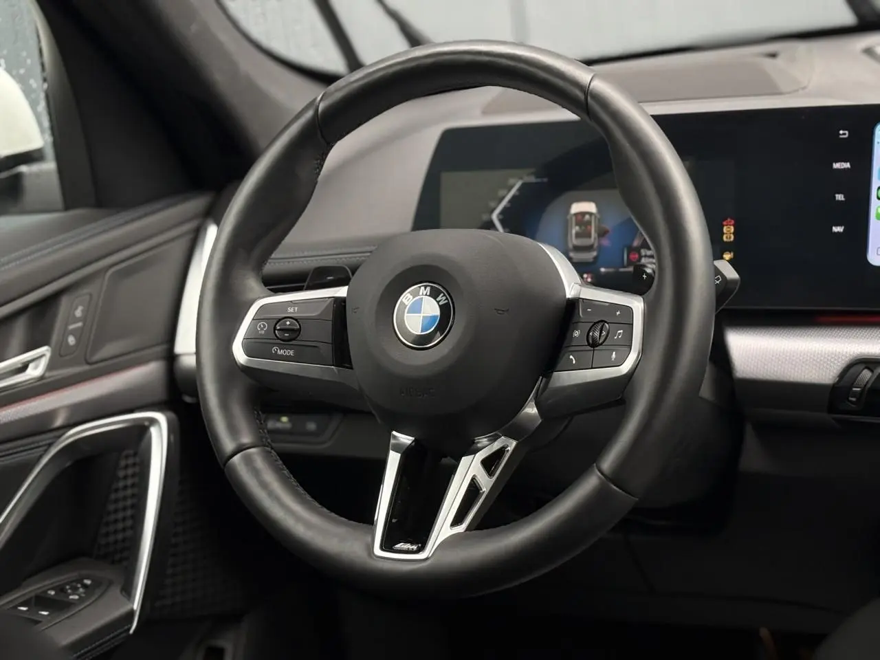 Vue rapprochée du volant cuir noir M avec commandes multifonctions du BMW X1 sDrive 20d blanc Mineral 2025.