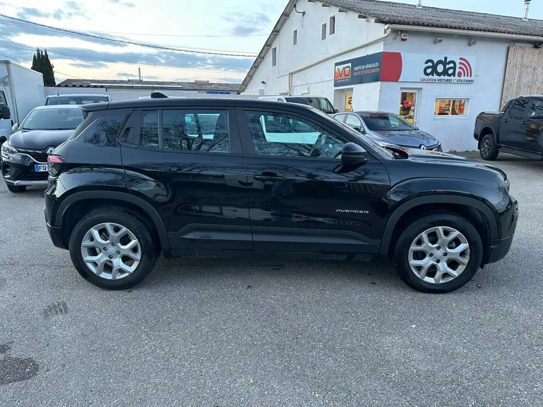 Vue de profil côté gauche d'un Jeep Avenger noir 2025 avec jantes alliage 17 pouces, garé devant un bâtiment commercial.