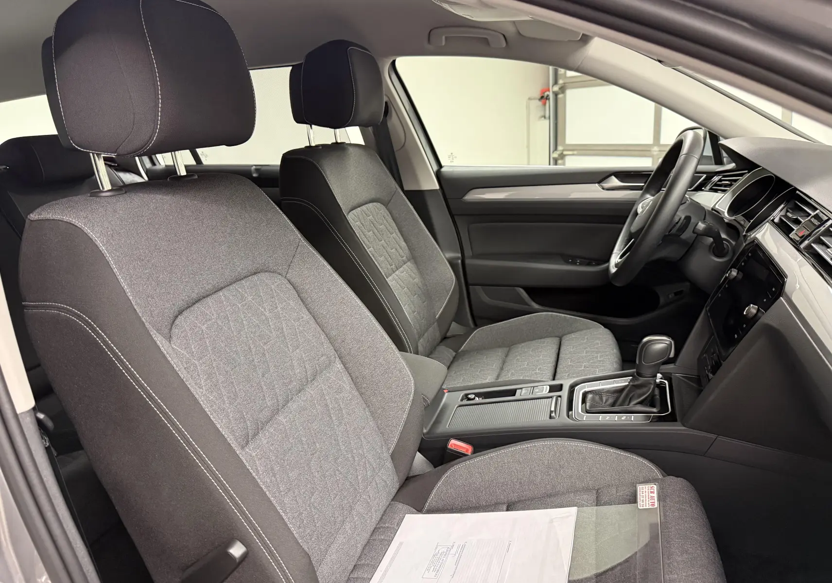 Vue intérieure côté droit de la Volkswagen Passat SW 2.0 TDI 122 DSG7 Business avec sièges tissu gris et console centrale noire.