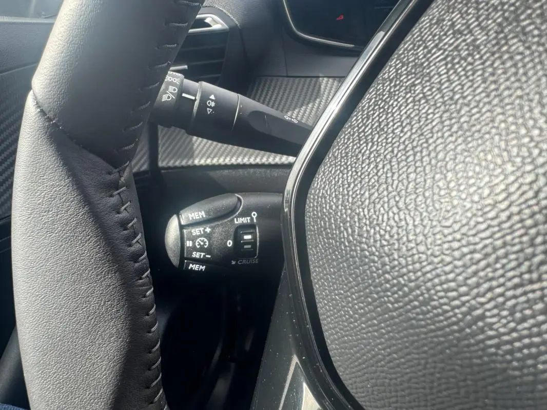 Gros plan sur la commande de régulateur de vitesse à gauche du volant en cuir noir du Peugeot 2008 blanc 2024.