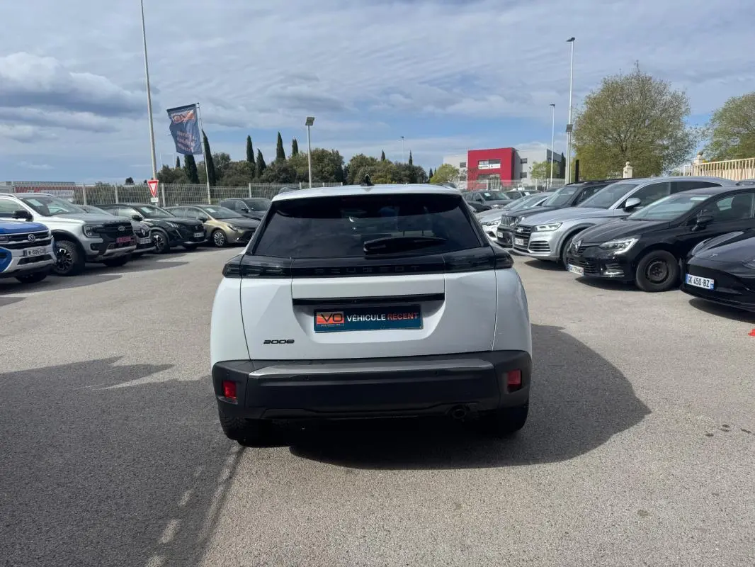 Vue arrière d’un Peugeot 2008 blanc 2024 avec feux noirs et lunette teintée, stationné en extérieur parmi d’autres véhicules.