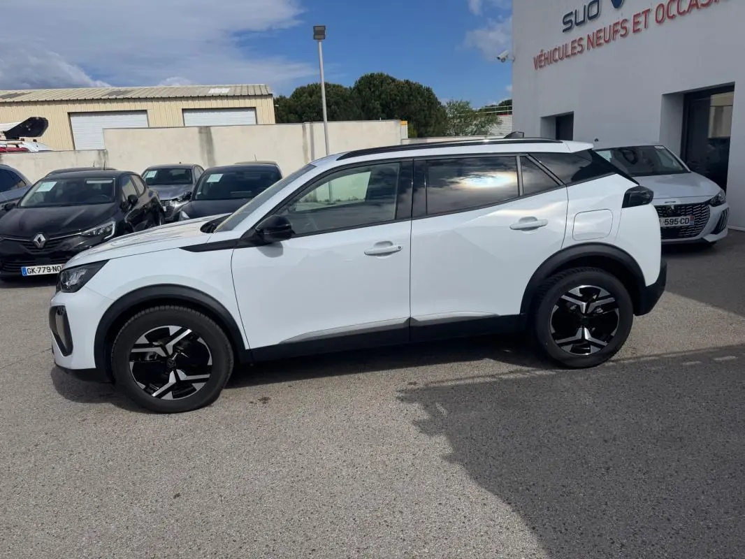 Peugeot 2008 blanc vue de profil côté gauche, avec jantes alliage noires et barres de toit visibles.